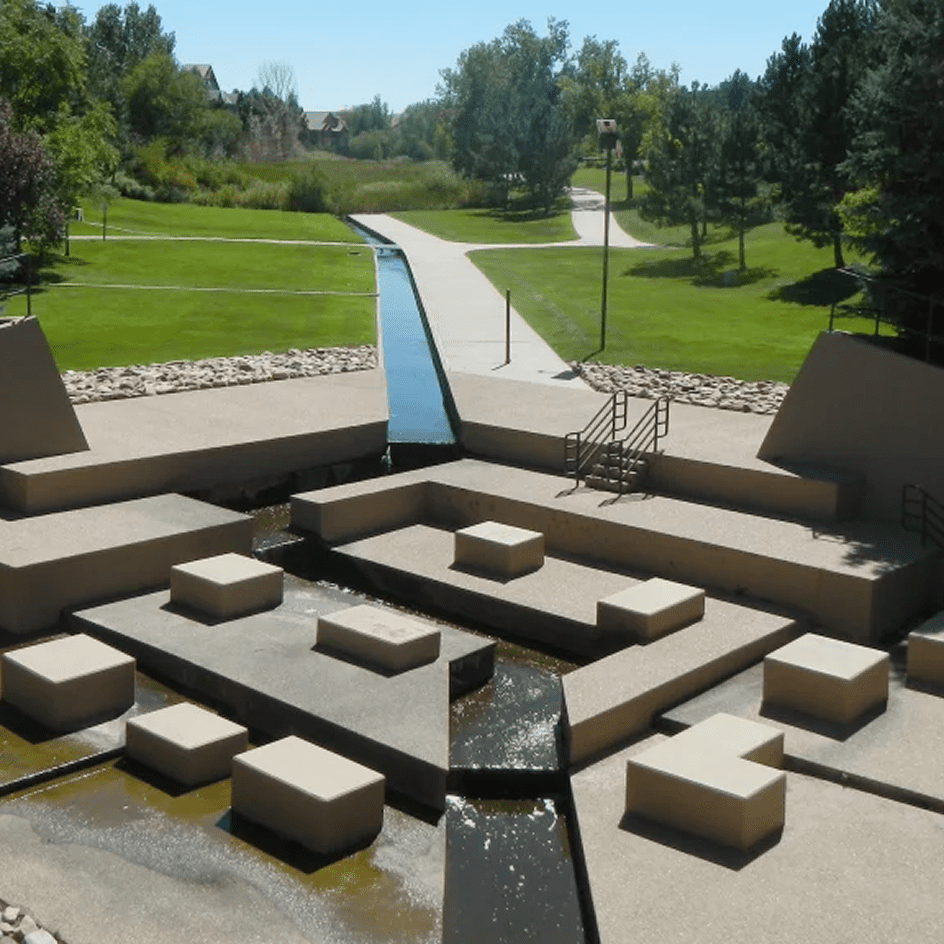 Landscaped public plaza with a geometric concrete water feature and green park in the background